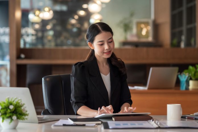 Beautiful young Asian businesswoman smiling sitting working on tablet in office. empresaria